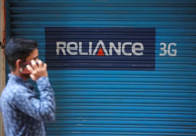 A man speaks on his mobile phone as he walks past a closed shop painted with an advertisement of Reliance Communications in Mumbai.(Reuters File Photo)