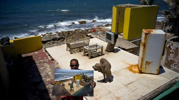 Roberto Figueroa stands eight months later, holding a photo taken on October 5, 2017 of him at his seaside home that was destroyed by Hurricane Maria, on the same property in Puerto Rico. Figueroa, who found a job at a pizzeria is aiming to rebuild his home and has re-appealed after his federal aid application was rejected twice. He visits his property daily to feed and take care of his pet dog. (Ramon Espinosa / AP)