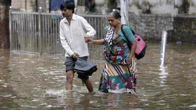 A man helps an elderly woman past a waterlogged street in Mumbai. Several parts of the city were flooded after moderate rainfall on Thursday. Parts of central Mumbai, Elphinstone Road, Parel, Dadar TT Circle and Dadar’s Hindmata had 1.5 feet of water. (Rajnish Kakade / AP)