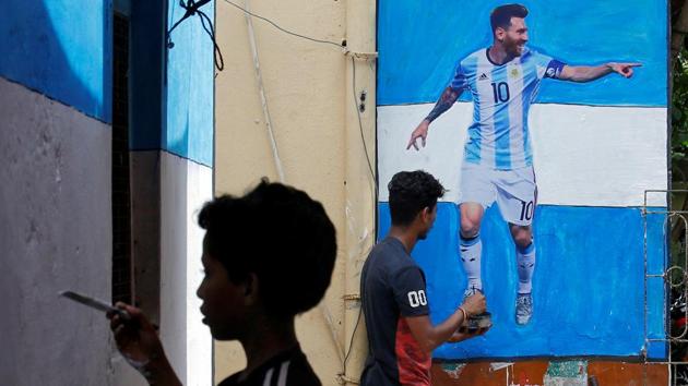 A boy paints a wall with the colours of Argentina's flag next to a man giving finishing touches to a cut-out of soccer player Lionel Messi. (REUTERS)