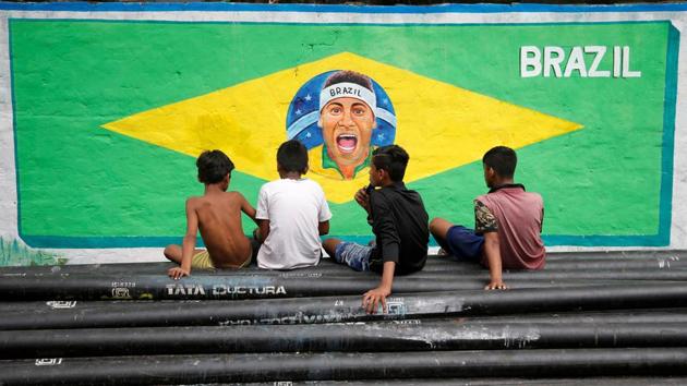 Boys sit on pipes in front of an image of Neymar painted on a wall along a road. (REUTERS)