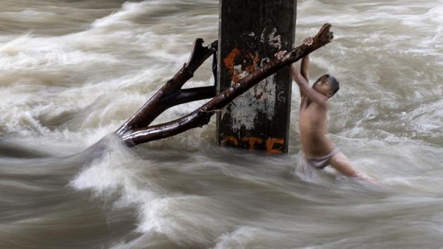 A boy holds a partially submerged branch as he plays in a swollen river caused by heavy rains under a bridge in Manila, Philippines. (Noel Celis / AFP) A boy holds a partially submerged branch as he plays in a swollen river caused by heavy rains under a bridge in Manila, Philippines. (Noel Celis / AFP)