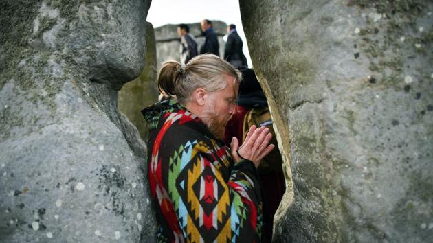 A man gestures between stones as the sun rises through the stones at Stonehenge as crowds of people gather to celebrate the dawn of the longest day in the UK, in Wiltshire, England. (Ben Birchall / PA via AP)