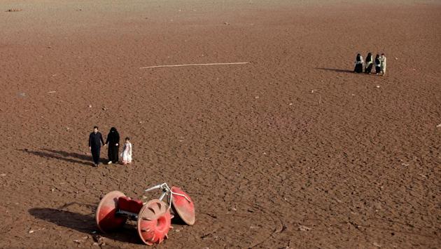 People walk near a three-wheeler parked at a dry portion of land that was once submerged underwater, at the bank of Rawal lake in Islamabad, Pakistan. (Faisal Mahmood / REUTERS)