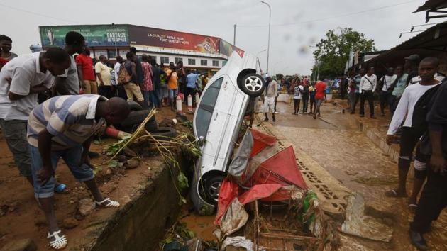Pedestrians look at the wreckage of a vehicle lodged in a storm drain on a street in Abidjan after floodwaters receded following an overnight downpour in the Ivory Coast’s economic capital. (Sia Kambou / AFP)