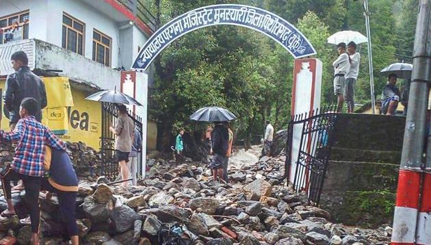 People stand on the rubble washed away by the flash floods after a cloudburst at Munsiyari in Pithoragarh district on Monday.(PTI)