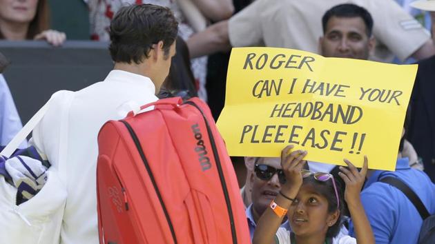 A fan holds a banner next to Roger Federer, asking for his headband at the end of his Men's Singles first round match against Serbia's Dusan Lajovic at the Wimbledon Tennis Championships in London on July 2, 2018.(AP)