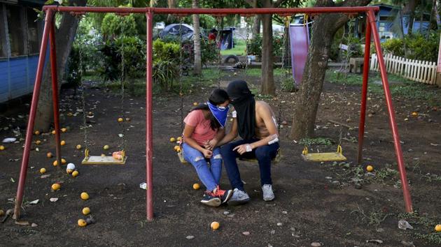 University students share a moment on a swing set inside the university. From the outside, the university looks like a fortress with approaching streets sprinkled with metal spikes to puncture tires. (Esteban Felix / AP)