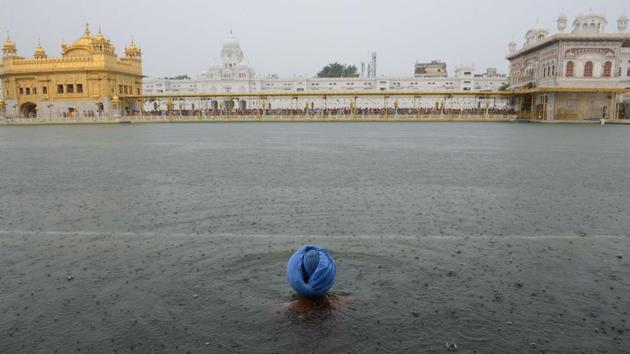 A devotee takes a dip in the holy sarovar (water tank) as it rains at the Golden Temple in Amritsar on July 3, 2018. (Narinder Nanu / AFP)