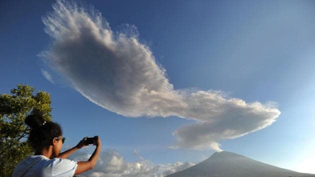 A woman takes photos as Mount Agung volcano sends up another plume of smoke, seen from the Kubu subdistrict in Karangasem Regency on Indonesia's resort island of Bali. (Sonny Tumbelaka / AFP)