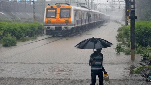 A man carrying an umbrella walks past a passenger train that moves through a water-logged track during heavy rains in Mumbai, July 9, 2018.(Reuters)