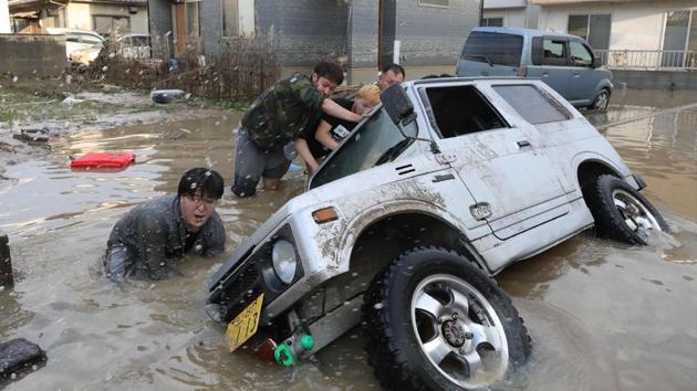 Residents try to upright a vehicle stuck in a flood hit area. The assessment of casualties has been difficult because of the widespread area affected. Officials in Ehime prefecture asked the central government to review a weather warning system, noting that rain warnings were issued after damage and casualties were occurring. (JIJI Press / AFP) Residents try to upright a vehicle stuck in a flood hit area. The assessment of casualties has been difficult because of the widespread area affected. Officials in Ehime prefecture asked the central government to review a weather warning system, noting that rain warnings were issued after damage and casualties were occurring. (JIJI Press / AFP)