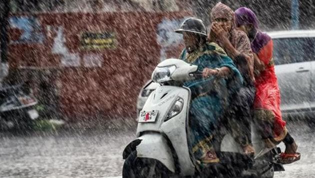 Commuters make their way across a street during heavy rain in Ahmedabad.(PTI Photo)