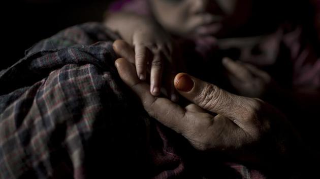 “S” holds her baby boy's hand as she sits in her shelter in Kutupalong refugee camp. A widow, “S” was so worried about her neighbours discovering her pregnancy that she suffered silently through labor in her shelter, stuffing a scarf in her mouth to swallow her screams. To give birth to a child without a husband was to invite admonishment. (Wong Maye-E / AP)