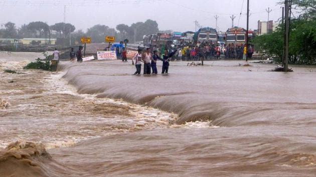 People make way through flood waters on the Una-Veraval highway after heavy rains, in Una town of Gir Somnath district on Tuesday, July 17, 2018.(PTI Photo)
