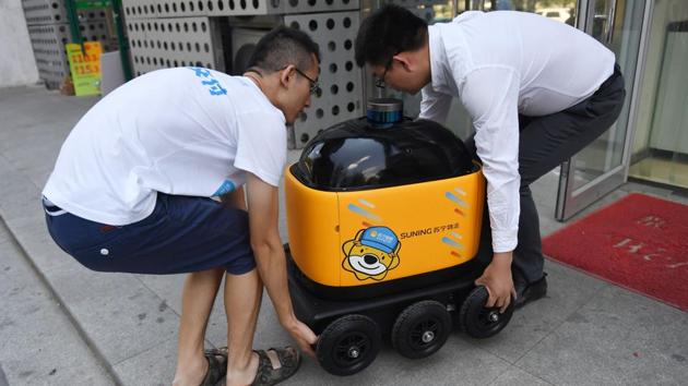 Liu Zhiyong (R) founder and CEO of Zhen Robotics, and a colleague carry a delivery robot out of a Suning supermarket. “At the moment, there are 100 million packages delivered every day in China. It will be one billion in the future,” Liu said. “There will not be enough humans to make the deliveries. We need more and more robots to fill this gap in manpower. And to reduce costs,” added the CEO. (Greg Baker / AFP) Liu Zhiyong (R) founder and CEO of Zhen Robotics, and a colleague carry a delivery robot out of a Suning supermarket. “At the moment, there are 100 million packages delivered every day in China. It will be one billion in the future,” Liu said. “There will not be enough humans to make the deliveries. We need more and more robots to fill this gap in manpower. And to reduce costs,” added the CEO. (Greg Baker / AFP)