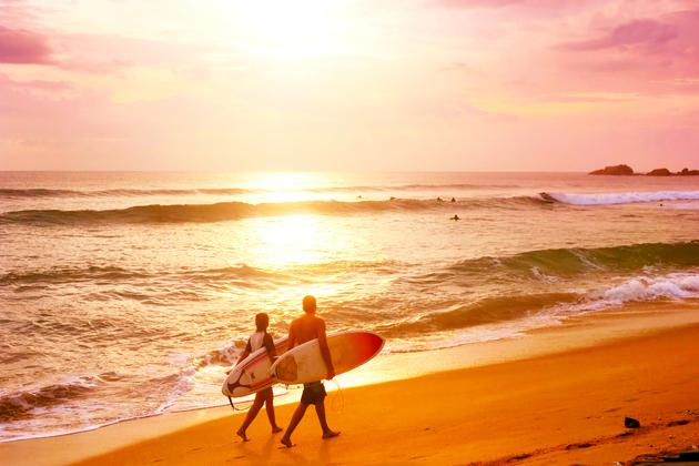 Surfers walks along the beach watching a scenic sunset in Hikkaduva, Sri Lanka. (shutterstock) 