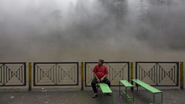 A man sits in front of a small lake covered in mist in Dharmsala, Himachal Pradesh on July 17, 2018. (Ashwini Bhatia / AP)