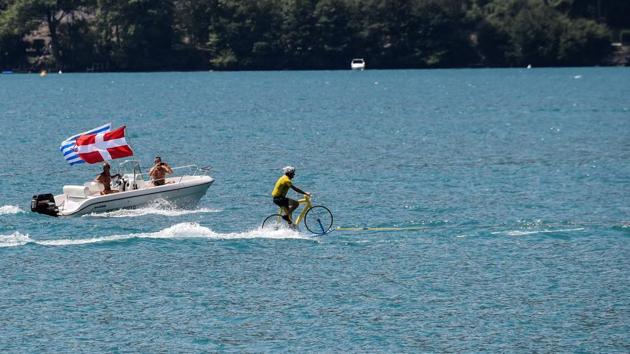 A man wearing a yellow jersey water skies on a bicycle on the Lake of Annecy during the tenth stage between Annecy and Le Grand-Bornand, French Alps, on July 17, 2018. (Jeff PACHOUD / AFP) A man wearing a yellow jersey water skies on a bicycle on the Lake of Annecy during the tenth stage between Annecy and Le Grand-Bornand, French Alps, on July 17, 2018. (Jeff PACHOUD / AFP)