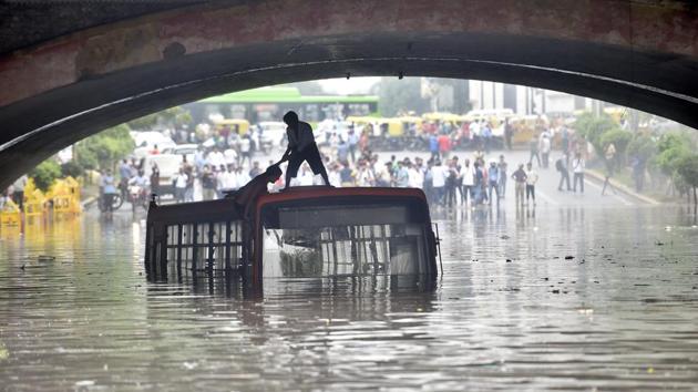 Two local boys climb on top of a bus after heavy rain inundated the road under the Shivaji Bridge, also known as Minto Road Bridge in New Delhi on July 16, 2018. (Ajay Aggarwal/HT PHOTO)
