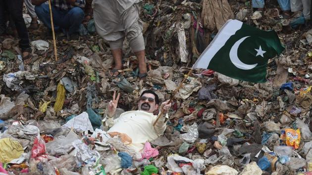 In this picture taken on July 9, 2018, Ayaz Memon Motiwala, 42, an independent Pakistani candidate contesting a seat in the National Assembly and two seats for the provincial Sindh Assembly, holds a Pakistan national flag as he lies partially submerged in garbage at a dump during an election rally in Karachi. (AFP) In this picture taken on July 9, 2018, Ayaz Memon Motiwala, 42, an independent Pakistani candidate contesting a seat in the National Assembly and two seats for the provincial Sindh Assembly, holds a Pakistan national flag as he lies partially submerged in garbage at a dump during an election rally in Karachi. (AFP)
