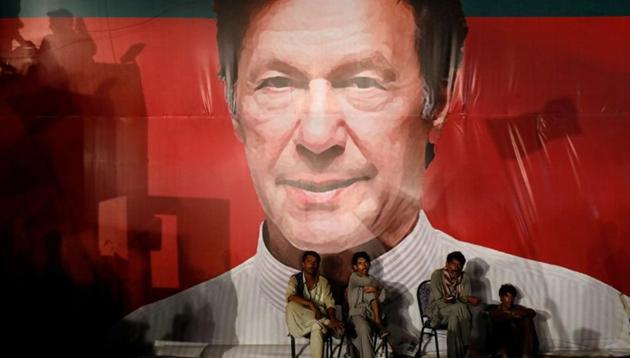 Workers, who set up the venue, sit under a wall with a billboard displaying photo of Imran Khan, chairman of the Pakistan Tehreek-e-Insaf (PTI), political party, as they listen to him during a campaign rally ahead of general elections in Karachi, Pakistan.(Reuters File Photo)