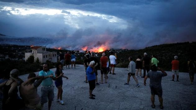 People watch a wildfire raging in the town of Rafina. At least six people died trying to escape the flames into the sea. Some 715 people were evacuated by boats to Rafina, the government said. (Alkis Konstantinidis / REUTERS) People watch a wildfire raging in the town of Rafina. At least six people died trying to escape the flames into the sea. Some 715 people were evacuated by boats to Rafina, the government said. (Alkis Konstantinidis / REUTERS)