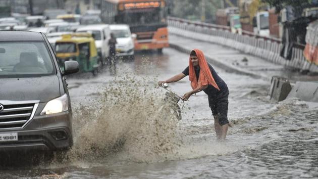 A man tries to save himself from a splash of water at Rohtak road near Anand Parbat. Residents of Delhi-NCR witnessed heavy rainfall on Thursday morning which led to waterlogging in several areas and brought rush-hour traffic to a virtual standstill. (Sanchit Khanna / HT Photo)