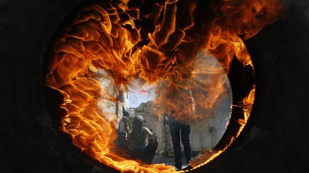 Palestinian protesters are seen through a burning tyre during clashes with the Israeli soldiers after the Friday prayers in the centre of the occupied West Bank city of Hebron on July 27, 2018. (Hazem Bader / AFP) Palestinian protesters are seen through a burning tyre during clashes with the Israeli soldiers after the Friday prayers in the centre of the occupied West Bank city of Hebron on July 27, 2018. (Hazem Bader / AFP)
