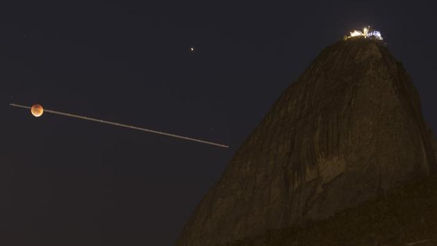In this time exposure, airplane navigation lights form a line crossing the blood moon, as it rises next to Sugar Loaf mountain in Rio de Janeiro, Brazil. (Leo Correa / AP)