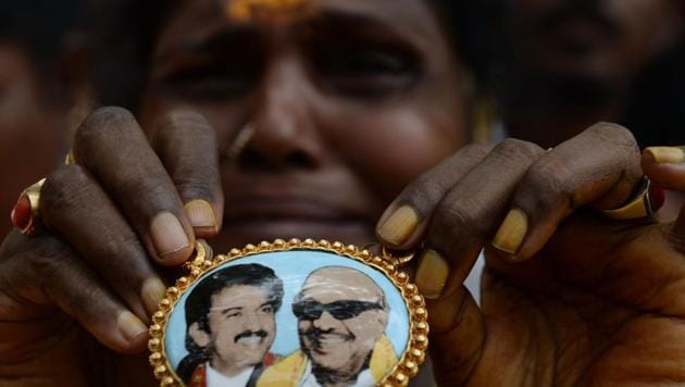 A DMK party supporter cries as she displays a locket with a portrait of party president M Karunanidhi n front of hospital where he is being treated in Chennai.(AFP Photo)