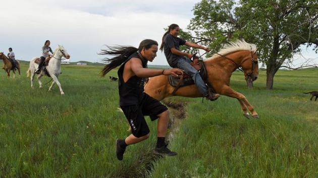 Mahto In The Woods jumps over a small creek on foot while his cousin Jayden Lookinghorse jumps over on his horse on the Cheyenne River Reservation. As it moved through Indian Country, the ride picked up Lakota, Dakota, Nakota, Arapaho and Cheyenne, all related tribes, all signers of the treaty. Some boys from Bridger joined with just the clothes on their backs. (Stephanie Keith / REUTERS)