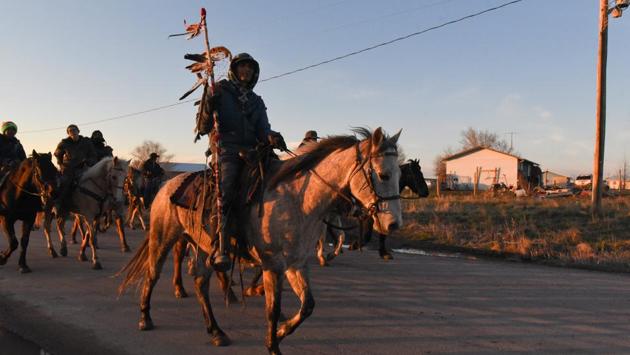 For two nights in Pine Ridge, accommodations were a middle school gym and campsite beside a reservoir. Moving on meant leaving “Lakota land” for Nebraska, where riders primarily rested on roadsides and relied on camp cooks for food. As the sun set, smoke rose from two kitchens, the flags of various groups were displayed and their leaders spoke. Later, children played with lassos. (Stephanie Keith / REUTERS)
