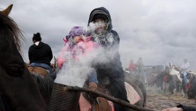 Austin Warrior, 11, and his sister Delores Warrior are covered with sage smoke in Harrison, Nebraska. Dawn and dusk during the ride found riders and horses in a circle waiting to be “smudged.” A person would pass with sage, thought to cleanse, smoking in a can. If it was morning, the riders would set out single file behind one rider carrying a sacred staff. At night, horses were corralled before dinner. (Stephanie Keith / REUTERS)