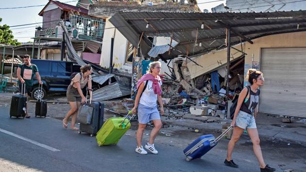 Tourists pull their suitcases as they walk past damaged buildings in Pemenang. Sutopo said there were no fatalities among the local and foreign tourists and a joint search and rescue team had deployed three ships to evacuate people. (Ahmad Subaidi / Antara Foto / REUTERS) Tourists pull their suitcases as they walk past damaged buildings in Pemenang. Sutopo said there were no fatalities among the local and foreign tourists and a joint search and rescue team had deployed three ships to evacuate people. (Ahmad Subaidi / Antara Foto / REUTERS)