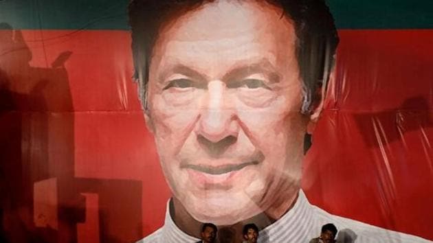 Labourers, who set up the venue, sit under a wall with a billboard displaying a photo of Imran Khan, chairman of the Pakistan Tehreek-e-Insaf (PTI), political party in Karachi, Pakistan.(Reuters) Labourers, who set up the venue, sit under a wall with a billboard displaying a photo of Imran Khan, chairman of the Pakistan Tehreek-e-Insaf (PTI), political party in Karachi, Pakistan.(Reuters)
