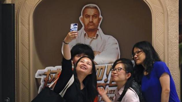 Chinese women take a selfie with a poster of Indian Bollywood blockbuster film "Dangal" on display at a cinema in Beijing on May 22, 2017.(AP File Photo)