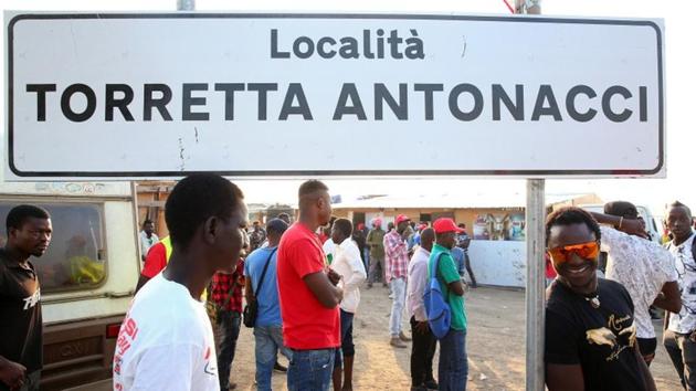 Labourers stand near a road sign reading “Torretta Antonacci place” outside the “Great Ghetto” near Foggia. Rather than employing pickers directly and putting them on regular contracts, farmers turn to caporali, or gangmasters, who gather labourers from various camps and ghettos and drive them to the fields in overcrowded vans. These middlemen hand out the wages, keep a handsome share for themselves, migrants say. (Alessandro Bianchi / REUTERS) 