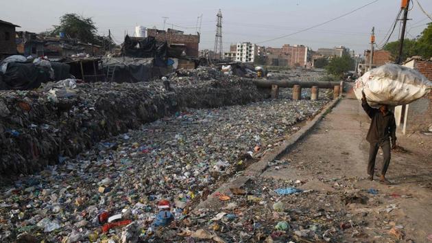 This file photo shows a man carrying a bag containing plastic recyclable items next to a sewage drain canal full of garbage in the Taimur Nagar slum area in New Delhi. (AFP Photo) This file photo shows a man carrying a bag containing plastic recyclable items next to a sewage drain canal full of garbage in the Taimur Nagar slum area in New Delhi. (AFP Photo)