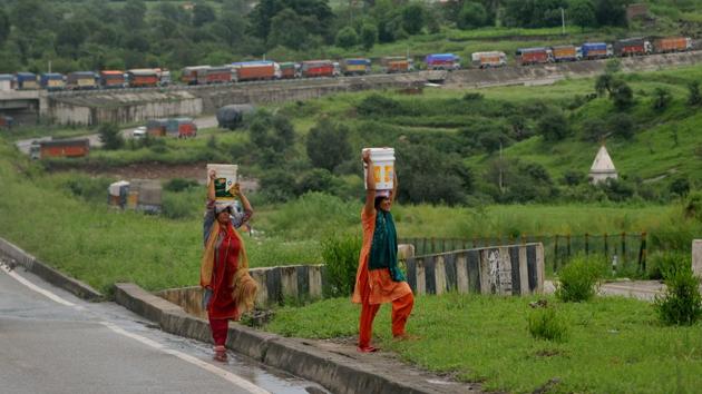 Women carry water buckets in the backdrop is seen stranded vehicles as they wait for the opening of the Jammu-Srinagar national highway which is closed to traffic due to landslide after heavy monsoon showers, at Udhampur about 65 km from Jammu. (Nitin Kanotra / HT Photo) 