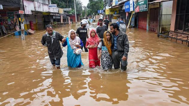 People wade across a waterlogged street after being rescued from flood-affected regions following heavy monsoon rainfall in Kochi on Saturday.(PTI Photo)