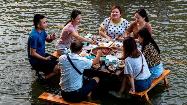 People eat hotpot at a table set up in a creek, inside a tourist attraction on a hot day in Chongqing, China. (REUTERS)