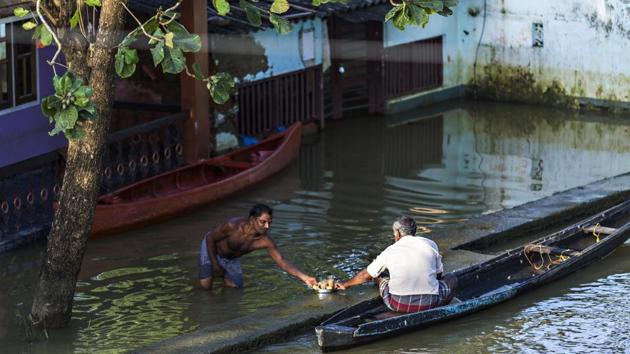 A man standing in floodwater shares a tray of tea with another man sitting in a canoe in Kainakary village in the district of Alappuzha, Kerala.(Bloomberg Photo)