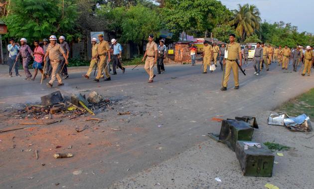 Security personnel walk past burnt ballot boxes lying on a road after violence during panchayat elections in Rampur in South Dinajpur district of West Bengal in May.(PTI)