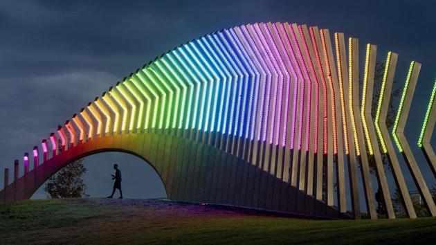 A man walks under Moving Surfaces, a giant steel and light sculpture at Ottawa’s Lansdowne Park, as it is lit up in the colours of the rainbow, during Pride Week. (Justin Tang / The Canadian Press via AP)
