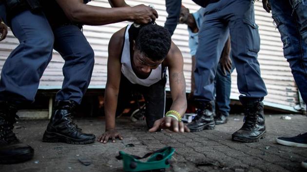 A suspected looter is detained by South African police officers as he emerges from a looted foreign-owned shop in Soweto, Johannesburg during unrest that erupted after a foreign shop owner allegedly shot and killed a member of the community during a demonstration. (Marco Longari / AFP)