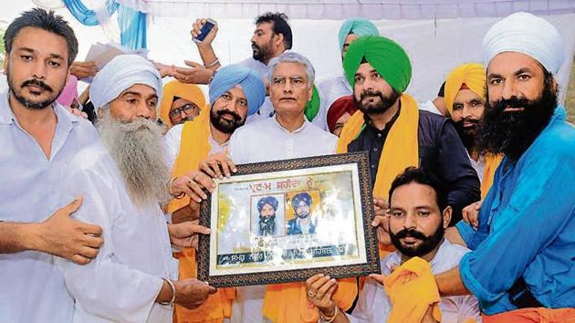 Punjab Congress chief Sunil Jakhar, flanked by ministers Balbir Singh Sidhu and Navjot Singh Sidhu, receives a memento carrying the photographs of the two victims of the Behbal Kalan police firing, at a rally in the village on Wednesday.(HT Photo)