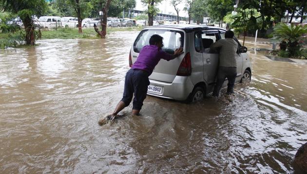 People push a car through a waterlogged street after heavy rains near Sector 32 in Gurugram on Wednesday.(Yogendra Kumar/HT Photo)