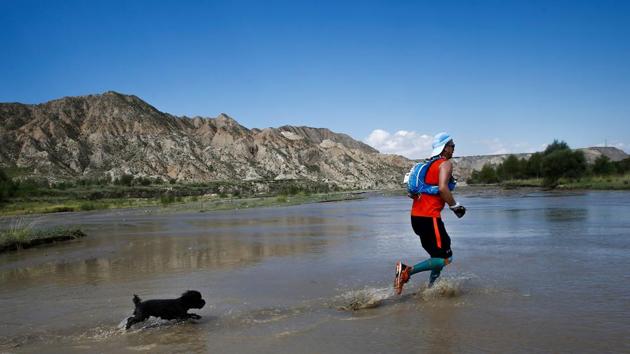 Trail runner Wang Yaoxing and his poodle Blackbean cross a stream that flows into the Longyangxia Reservoir. “When I arrived, I thought Longyangxia was quite remote; the scenery was beautiful but it was isolated and economically lagging,” said Ying Miyan, chairman of China’s largest salmon fishery, Qinghai Minze Longyangxia Ecological Aquaculture Co., which sponsored the challenge. (Thomas Peter / REUTERS) Trail runner Wang Yaoxing and his poodle Blackbean cross a stream that flows into the Longyangxia Reservoir. “When I arrived, I thought Longyangxia was quite remote; the scenery was beautiful but it was isolated and economically lagging,” said Ying Miyan, chairman of China’s largest salmon fishery, Qinghai Minze Longyangxia Ecological Aquaculture Co., which sponsored the challenge. (Thomas Peter / REUTERS)