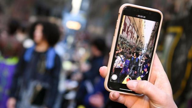 A woman takes a photo on her phone of models parading outfits by Australian label Asiyam during a Melbourne Fashion Week show in an inner-city laneway. (William West / AFP) A woman takes a photo on her phone of models parading outfits by Australian label Asiyam during a Melbourne Fashion Week show in an inner-city laneway. (William West / AFP)